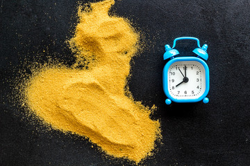 Deadline concept. Clock near sand on black background top-down