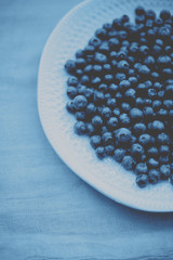 Blueberries in a plate on a table with a colored cloth.