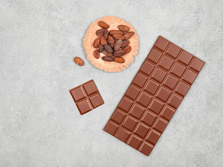 Bar of milk chocolate and cocoa beans on gray stone background