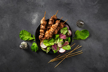 Chicken shish kebab with salad in plate on dark background top view
