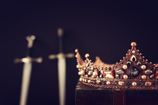 low key image of beautiful queen/king crown over antique box and sword. fantasy medieval period. Selective focus