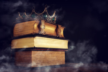 low key image of beautiful queen/king crown over old book and wooden table. vintage filtered....