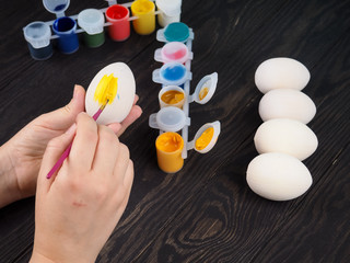 Close-up of woman hands painting an easter egg on wooden background. Female hands painting wooden easter egg with brush. the concept of handmade and Easter