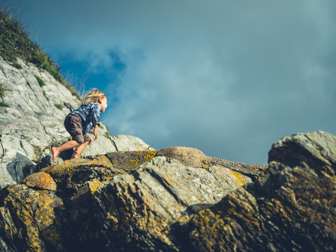 Little toddler climbing rock on the coast