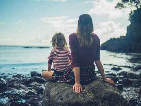 Mother and toddler sitting on a rock by the sea