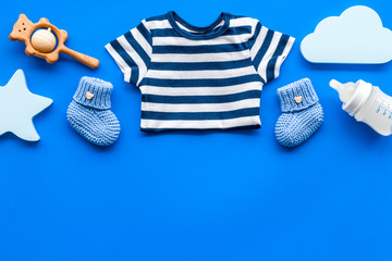 Newborn baby boy set - blue clothes as bodysuit, booties, toys - on blue table top-down frame copy space