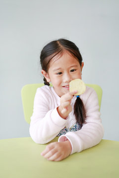 Portrait Of Happy Little Asian Child Girl Eating Crispy Potato Chips On White Background. Kid Enjoy Eating Concept.