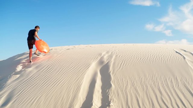 Happy man on sand in white sands dunes national monument park in New Mexico on disk sled sliding down hill panning pov