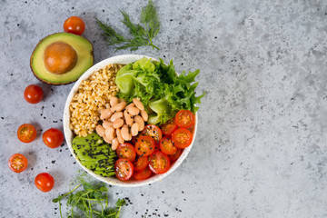 A plate of fresh salad with white beans, bulgur, cherry tomatoes and avocado, decorated with black sesame seeds. Horizontal photo with copy space, top view
