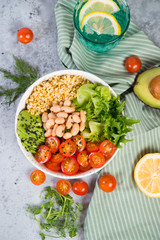 Fototapeta na wymiar A plate of fresh salad with white beans, bulgur, cherry tomatoes and avocado, decorated with black sesame seeds with products around the plate. Vertical photo, top view