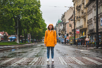 Fototapeta na wymiar woman in the middle of the street crossing road in yellow raincoat
