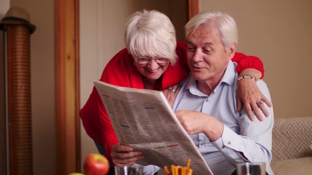 Happy senior couple reading newspaper at home