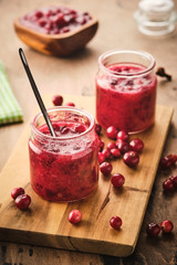 Cranberry jam in a glass jar on a wooden board.