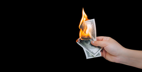 Human hand holding a burning 100 dollar bill. Black background. Close up, copy space.