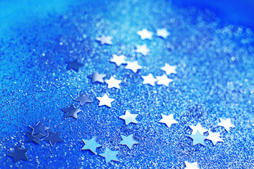 Splash of silver sparkles and stars on blue background. Blurry image. Selective focus.
