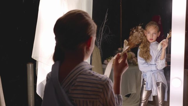 Young girl actress rehearsing with flower bouquet front mirror in dressing room. Girl teenager dancing with bouquet in dressing room front lighting mirror
