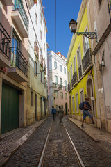 Lisbon, Portugal - 10/20/2018: Narrow street in old town of Lisbon, Portugal. Tourists in historical district of Lisboa. Colorful cityscape at sunny summer day. Lisbon scenic landmark. 