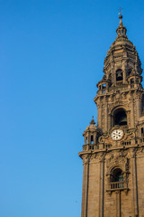 Fototapeta premium Santiago de Compostela, Spain -10/19/2018: Clock tower with bell and cross on clear blue sky background. Exterior of famous cathedral on sunny day. Ancient religious architecture. Unesco heritage.