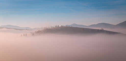 Top of the hill wrapped with the morning fog at Carpathian mountains. Beautiful sunrise over mountain.