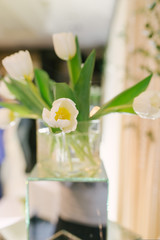 Fototapeta na wymiar Bouquet of white tulips in a glass vase in the interior decor or wedding. Selective focus