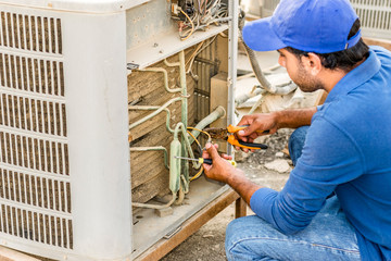 a professional electrician man is fixing the heavy unit of an air conditioner at the roof top of a...