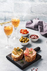 Wholegrain bread sandwiches with cream cheese, bacon and olives on a wooden cutting Board. A glass of white wine. Gray concrete background with Copy space.