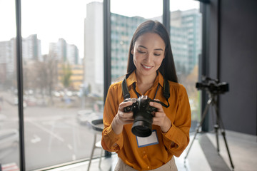 Dark-haired young cute reporter watching photos in camera