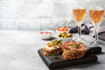 Wholegrain bread sandwiches with cream cheese, bacon and olives on a wooden cutting Board. A glass of white wine. Gray concrete background with Copy space.