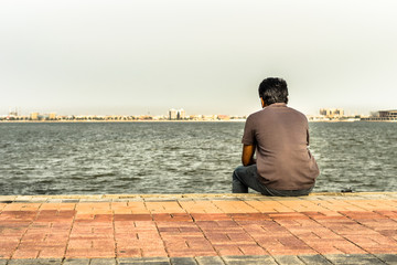 Fototapeta premium a lonely man is sitting on the rocks after divorce at seaside wearing grey t shirt and blue jeans in the bright cloudy day