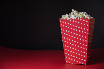frontal view of popcorn in white dotted red popcorn box on a red floor with a black background