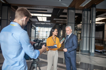 Asian female reporter standing next to grey-haired man
