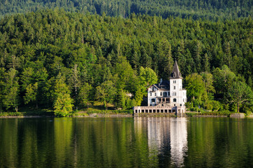 Fototapeta na wymiar A large white house in the form of a castle on the shore of the lake. Green mountains in the background.