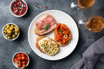Wholegrain bread sandwiches with cream cheese, bacon and olives canned peppers with tomato on a plate. Dark concrete background with Copy space.