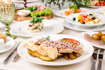 Served for holiday banquet restaurant table with grilled kebab meat, hot snack, dishes, salads, wine and water glasses. Table set for an event party in restaurant background