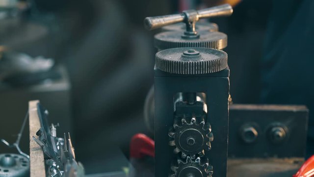 CU: young silversmith processes long metal silver cable with forge-rolling machine tool at workplace in workshop close view