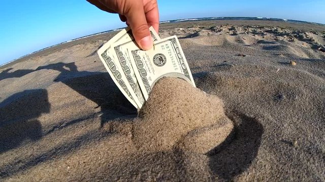 A girl takes out from the sand money notes of three hundred dollars.