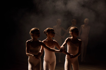 A group of small ballet dancers rehearses on stage with light and smoke