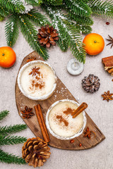 Fototapeta na wymiar Eggnog with cinnamon and nutmeg for Christmas and winter holidays. Homemade beverage in glasses with spicy rim. Tangerines, candles, gift. Stone concrete background