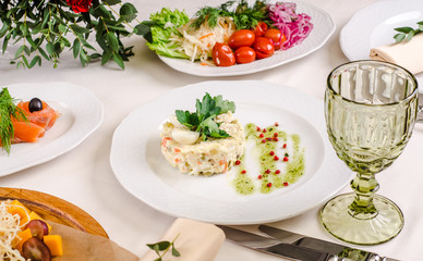 Russian salad served green onions on plate for catering. Top view banquet table with cold snacks on white tablecloth background. Party food concept.