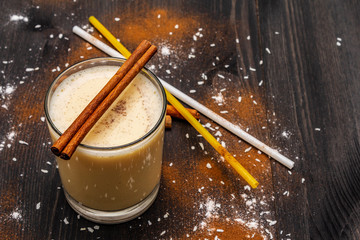 Traditional winter eggnog with milk, rum and cinnamon, sprinkle with grated nutmeg. Cocktail straws, dark wooden background