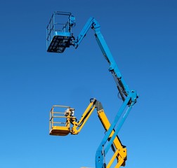 Two aerial work platforms, one over the other, against cloudless blue sky