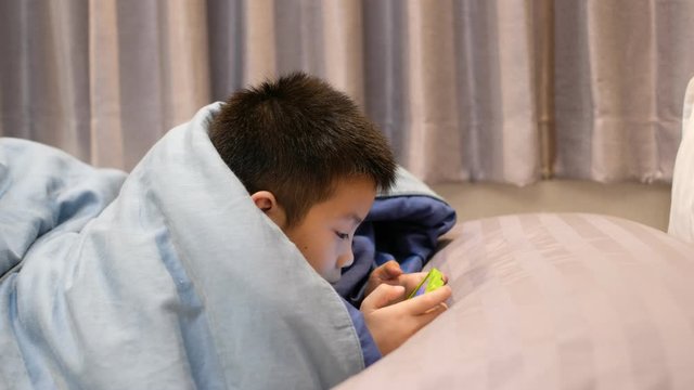 asian chinese boy playing smartphone on bed, kid use phone and play game, addicted game and cartoon, 