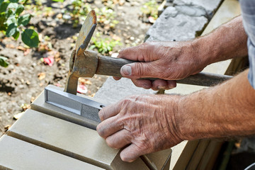 Bricklayer installing bricks on the new fence from facing bricks using hammer and building level.