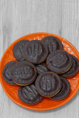 Jaffa cakes biscuits stacked on an orange plate.  On a grey wood surface.