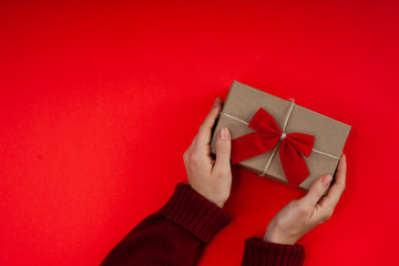 Female hands holding present with red bow on red background. Bright festive backdrop for holidays: Valentines day, Christmas, New Year. Flat lay