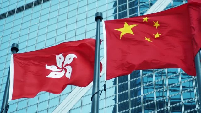 Hong Kong Flag and China Flag Waving in The Wind Against Office Building Together. Hong Kong and Mainland China Conflict Concept slow motion