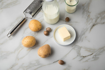 Kartoffeln, Milch, Salz, Butter, Muskatnuss als Zutaten mit Kartoffelpresse und Muskatreibe für Kartoffelpüree auf hell Marmor Hintergrund