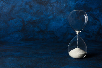 Time is running out concept. An hourglass with oozing sand, on a dark blue background with copyspace