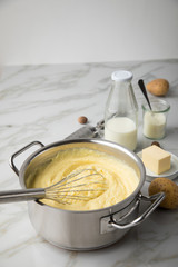 Kochtopf mit Kartoffelpüree mit Zutaten aus Kartoffeln, Milch, Salz, Butter, Muskatnuss dazu Muskatreibe und Schneebesen auf hell Marmor Hintergrund