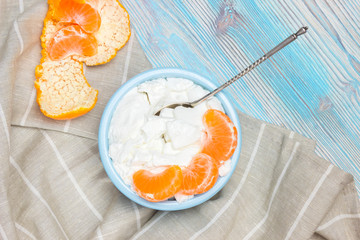 An overhead photo of fresh homemade cottage cheese and tangerine slices in the teal blue ceramic bowl. Fermented product with Lactose. Organic eco healthy meal, dairy fresh milk products. Top view.